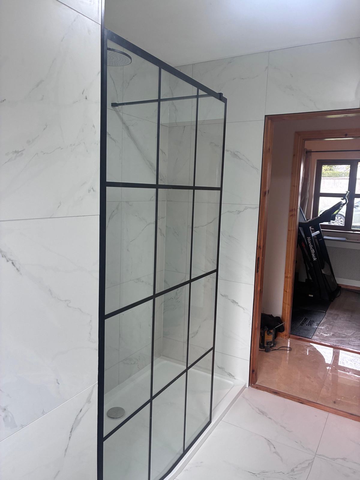 Walk-in shower with black grid screen and white marble-effect tiles
