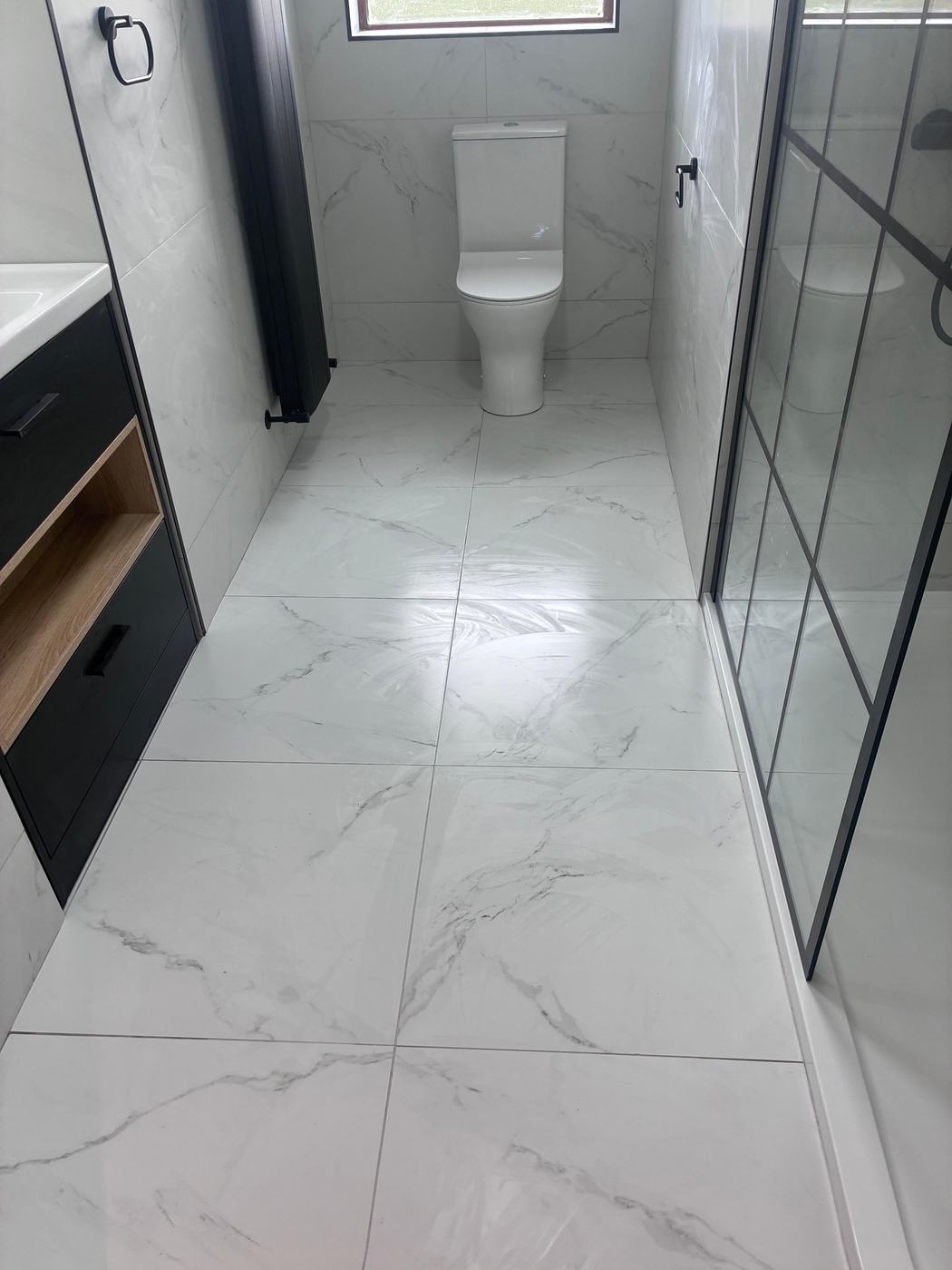 White marble-effect large-format floor tiles with black grid shower screen