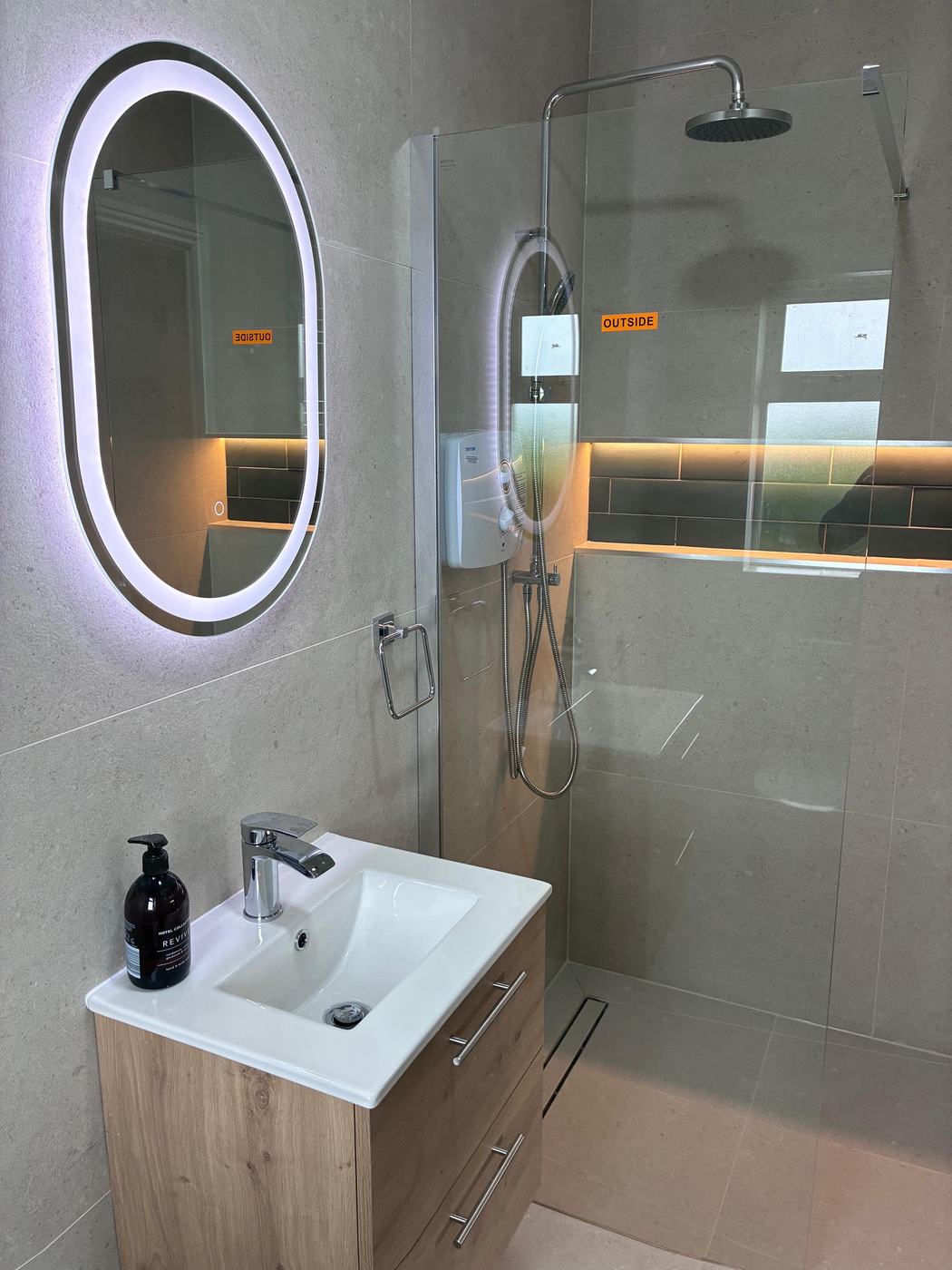 Stone-effect en-suite with backlit oval mirror, oak vanity, LED-lit niche and linear drain